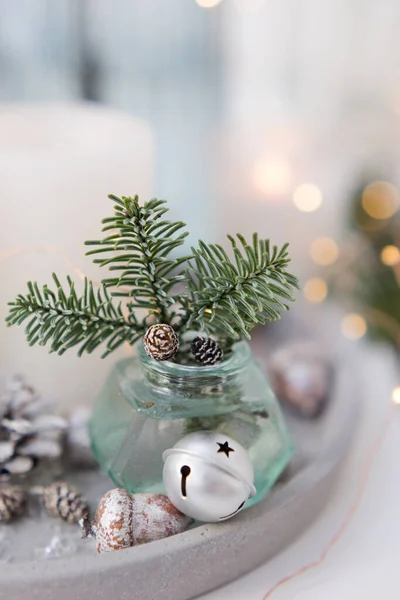 Bouquet of green spruce branches in vase, white burning candles and silver christmas bells at concrete tray