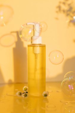 Sarı kozmetik şişesi, çiçekler, sabun köpükleri ve yağ damlaları sarı arka planda, kopyalama alanı ile maket