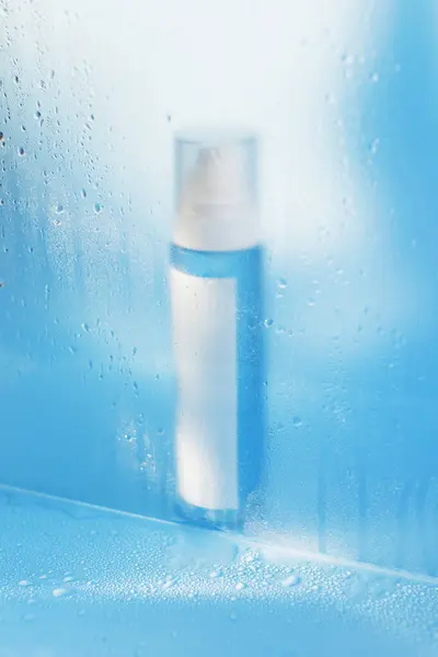 Blue cosmetic bottle with water drops on a blue background, mockup with copy space