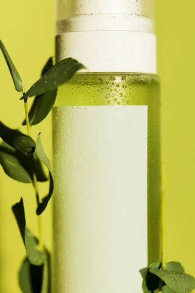 Green cosmetic bottle with water drops and eucalyptus leaves on a green background