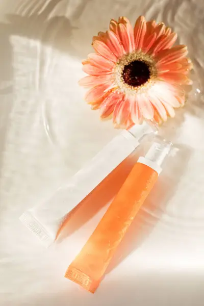 White and orange cosmetic tube, orange flower gerbera lies in the water with waves