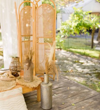 Rattan katlanır ekran ayırıcı ve arka bahçedeki pirinç vazolarla dolu bir masa.