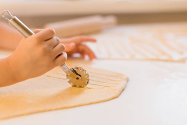 Çocuk mutfakta beyaz bir masada ev yapımı makarna yapıyor.