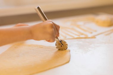 Çocuk mutfakta beyaz bir masada ev yapımı makarna yapıyor.