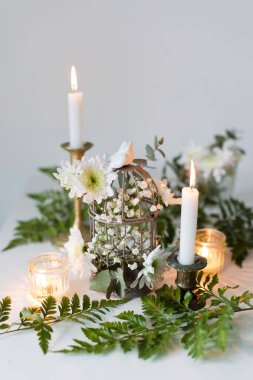 Beyaz arka planda kuş kafesi ve çiçekler olan güzel bir dekorasyon.