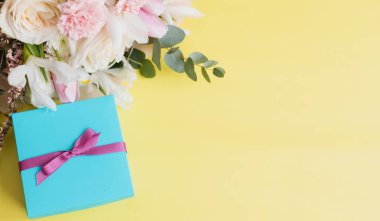 Beautiful bouquet with roses, carnations, iris and eucalyptus and blue gift box with pink ribbon on a yellow background, copy space. Mothers day, 8 march, holiday gift concept