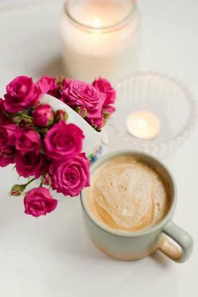 Cup with coffee, pink roses flowers and burning candles on a white background, copy space