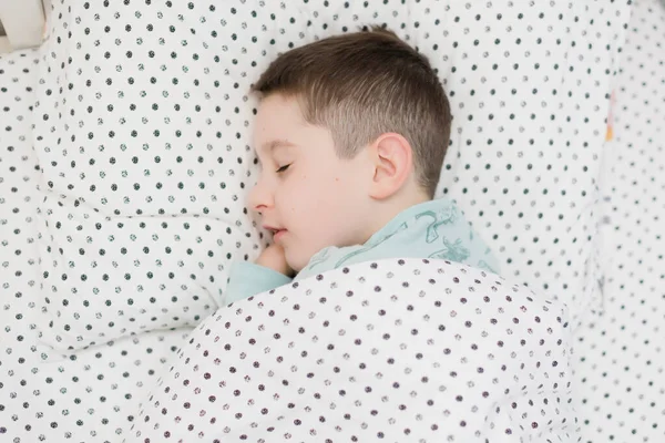 Mavi pijamalı, yatağında uyuyan beyaz çocuk.