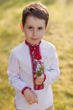 Geleneksel Ukraynalı beyaz çocuk vyshyvanka elinde bir buket mavi çiçekle beni unutma. Ukrayna etnik kostümü, çocuk vatansever elbisesi giyiyor.