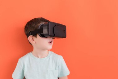 Sanal gerçeklik gözlüklü beyaz çocuk. Fotokopi alanı olan turuncu bir arka planda.