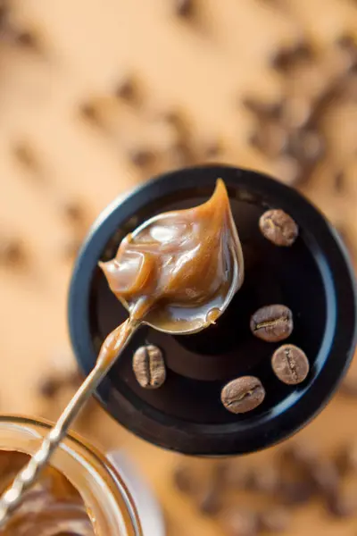 Jar with caramel sauce, metal vintage spoon and coffee beans on a brown background. Coffee caramel sauce taste