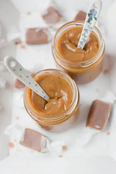 Jars with caramel sauce and caramel candy in paper wrapping lying on a white wooden tray