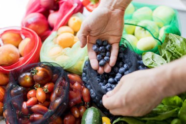 Tekstil eko torbalarında çeşitli meyve ve sebzeler. Çevre dostu, doğa koruma kavramı. Çiftlik pazarı, market teslimat konsepti. Adam böğürtlenli çanta tutuyor.