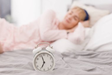 Beyaz saat ve pembe pijamalı bir kadın yatakta uyuyor.