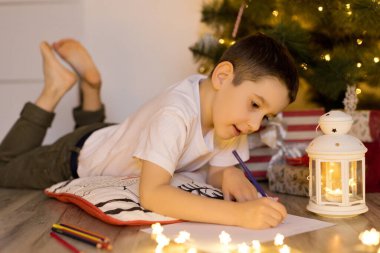 Çocuk Noel ağacının yanında yatıyor ve Noel Baba 'ya mektup yazıyor.