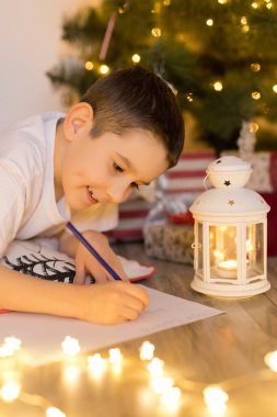 Çocuk Noel ağacının yanında yatıyor ve Noel Baba 'ya mektup yazıyor.