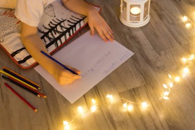 Çocuk Noel ağacının yanında yatıyor ve Noel Baba 'ya mektup yazıyor.