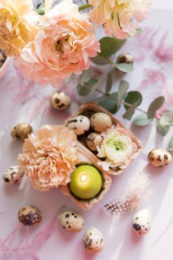 Paskalya konsepti, bıldırcın yumurtası, çiçekler ve mor arka planda yanan mum.