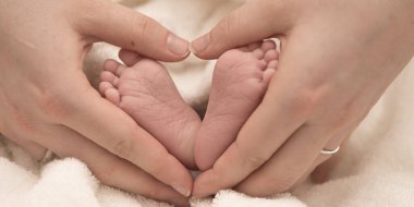 familiar hands and legs. happy mother forms a heart around the legs of her newborn tiny baby. 