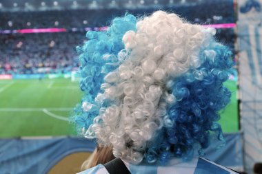 Arjantin Avustralya maçından sonra futbol taraftarı, futbol takımının renkleri ve açık havada Arjantin bayrağı bulunan tişört ve kıvırcık peruk giymiş dev bir televizyon ekranının önünde boş bir kampla stadyuma bakıyor.. 