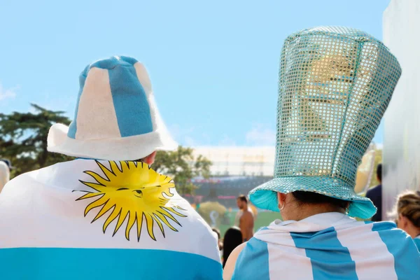 Arjantin milli takımının Buenos Aires 'teki açık hava parkında dev bir ekranda gösterilen maçını, sırtlarında tişört, kep ve ulusal bayrak olan kadın ve erkek futbol hayranları izliyor. 