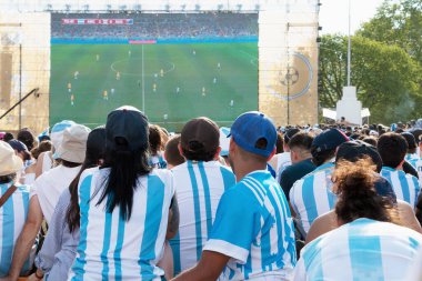Crowd of argentinian fans  dressed with argentina national team tshirt, sitting front a giant screen with the argentina football game in a popular projection