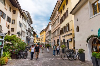 Bolzano, Italy - Aug 23, 2019 - People walking down the narrow street after rain clipart