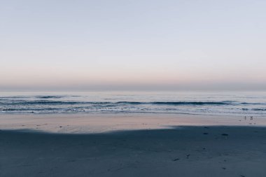 Sahilde sakin bir gün doğumu. Arka planda pembe gökyüzü.