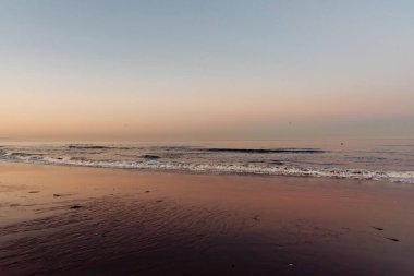 Sahilde sakin bir gün doğumu. Arka planda pembe gökyüzü.