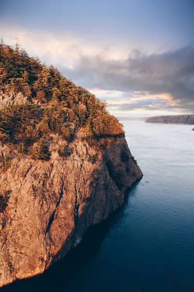 Gün batımı okyanusta kayalık bir dağı aydınlatıyor.