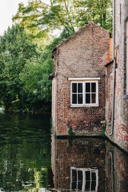 Yıpranmış duvarları olan eski tuğla bina, sakin bir kanalın yanında duruyor. Yapıyı, eski tuğlalarla çelişen yemyeşil alan sararken, bazı beyaz çerçeveli pencereler de kırsal cepheleri noktalıyor..