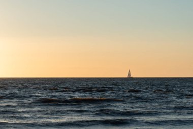 Ufukta yelkenli bir tekneyle denizde parlak bir günbatımı.
