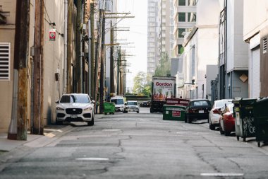 Vancouver, Kanada - 2 Haziran 2023 - Park etmiş araçların, bir dağıtım kamyonunun ve elektrik direklerinin yer aldığı hareketli bir şehir geçidi modern yüksek binaların arka planına karşı. Sahne, şehir hayatının dinamik ve faydacı özünü yakalar.