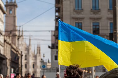 MILAN, İtalya - 25 Şubat 2023: Rusya-Ukrayna savaşından bir yıl sonra, birinci yıl dönümü. Ukrayna 'nın sarı ve mavi çizgili bayrağı mavi gökyüzü ve güneşle rüzgarda dalgalanıyor. Arka planda Milano 'daki Duomo katedrali var..