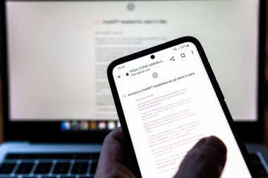 ITALY - 4 Nisan 2023: Akıllı telefon elinde ve ekranda ChatGPT 'nin İtalyan Guarantor tarafından İtalyan kullanıcıları için devre dışı bırakıldığını duyurdu. Açık Ai resmi sitesi ile bulanık dizüstü bilgisayar.