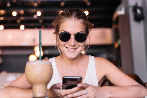 Portret Szczęśliwej Kobiety Używającej Telefonu Komórkowego Kawiarni Podczas Picia Frappe — Zdjęcie stockowe