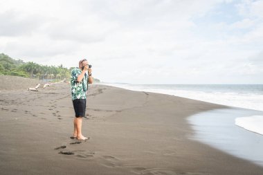 Sakin bir plajda dijital kamerayla fotoğraf çeken bir adamın fotokopi alanı.