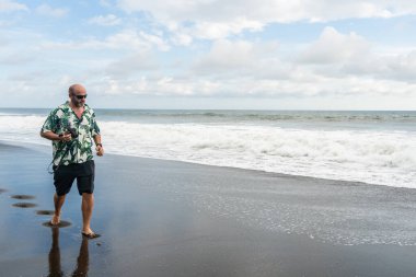 Fotoğraf makinesi ile kumlu bir plajda yürüyen bir adamın fotokopi alanı.
