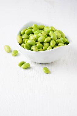 Beyaz ahşap masa üzerinde edamame tanecikleri olan, dikey, fotokopi alanı olan beyaz kase yakın plan.