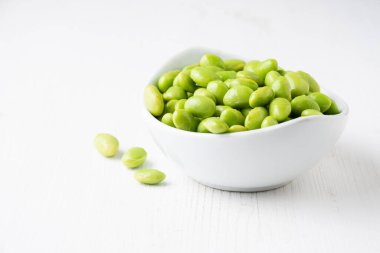Beyaz kâse görüntüsü beyaz ahşap masa üzerinde edamame tanecikleri, yatay, kopyalama alanı ile