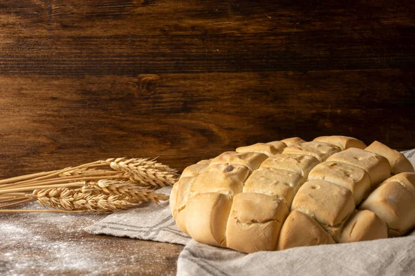 stock image Top view of ears of wheat and loaf of white bread on kitchen towel and dark wooden table with flour, horizontal, with copy space