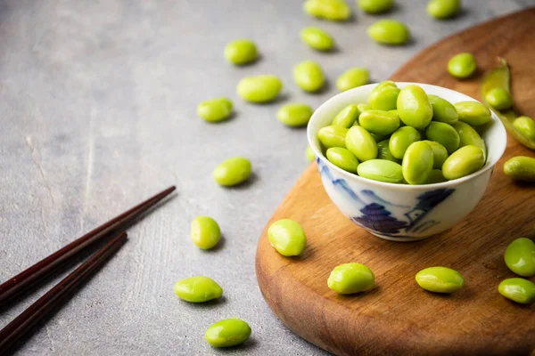 Tahta üzerinde yemek çubukları olan edamame tanecikli kasenin üst görüntüsü, seçici odak, gri arka plan, yatay