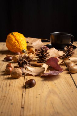 Kurumuş meyve, balkabağı, bir fincan kahve ve tarçın, ahşap masa üzerinde sonbahar yaprakları, siyah arka plan, dikey