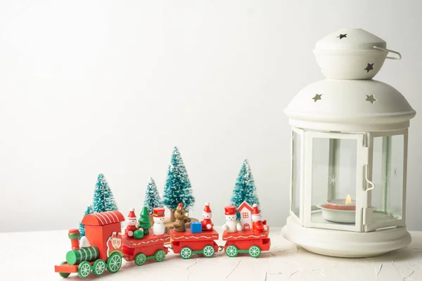 Close-up of white lantern with wooden Christmas train with dolls and small trees on white table, white background, horizontal, with copy space