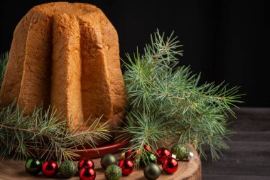 Pandoro 'nun, dalları ve Noel süslemeleri olan ahşap masadaki üst görüntüsü, siyah arkaplan, yatay, kopyalama alanı olan
