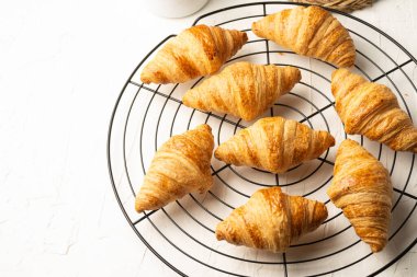 Top view of small croissants on round black rack and white table, horizontal, with copy space