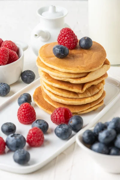 Close-up of pancakes in stack with blueberries and raspberries on table and white background, selective focus, vertical