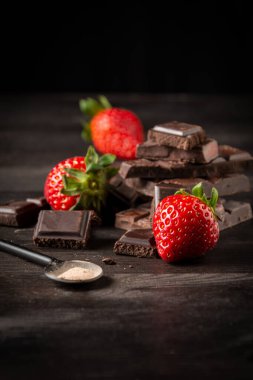 Koyu ahşap masa üzerinde çilekli çikolata parçaları ve kaşık görüntüsü, siyah arkaplan, dikey, kopyalama alanı