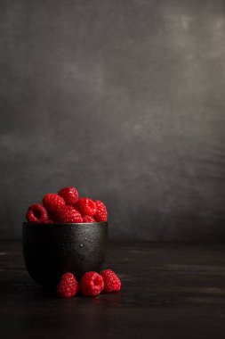 Koyu renkli masada kırmızı ahududu ve üç ahududu, koyu gri arkaplan, fotokopi alanı ile dikey.