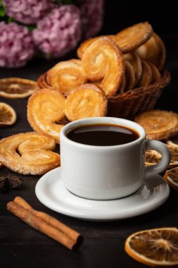 Bir fincan kahveye yakın poğaça, tarçın çubuğu ve eflatun çiçekleri koyu ahşap masada, fotokopi alanı ile dikey.